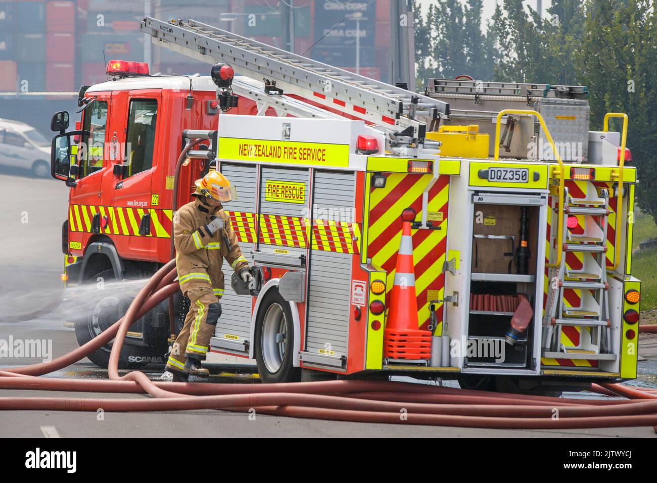 Un vigile del fuoco che lavora accanto a un motore antincendio con tubi flessibili in una scena di un incendio. Foto Stock
