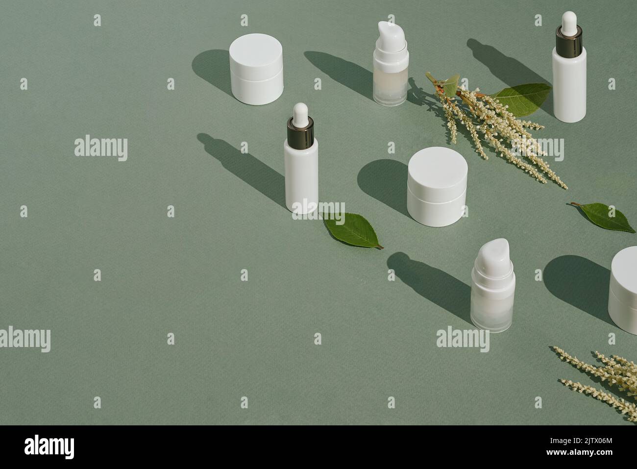 Mockup bianchi di imballaggi cosmetici e piante su sfondo verde con spazio copia. Siero, crema, lozione. Il concetto di cosmetici naturali e pelle Foto Stock