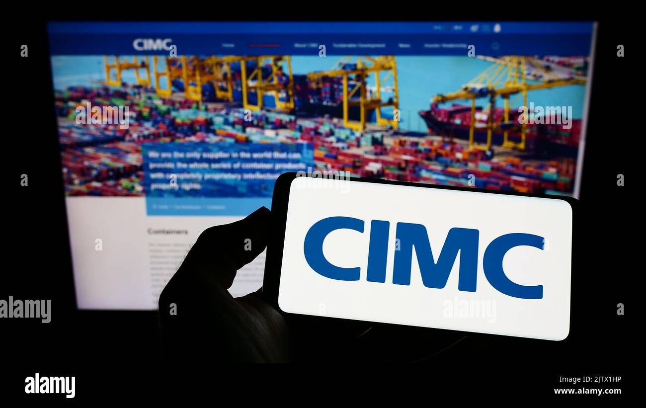 Persona che tiene il cellulare con il logo di China International Marine Containers (CIMC) sullo schermo di fronte al sito web aziendale. Messa a fuoco sul display del telefono. Foto Stock