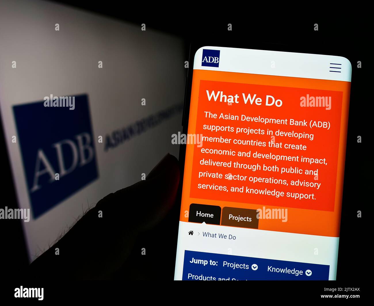 Persona che tiene il cellulare con pagina web dell'organizzazione Asian Development Bank (ADB) sullo schermo di fronte al logo. Messa a fuoco al centro del display del telefono. Foto Stock
