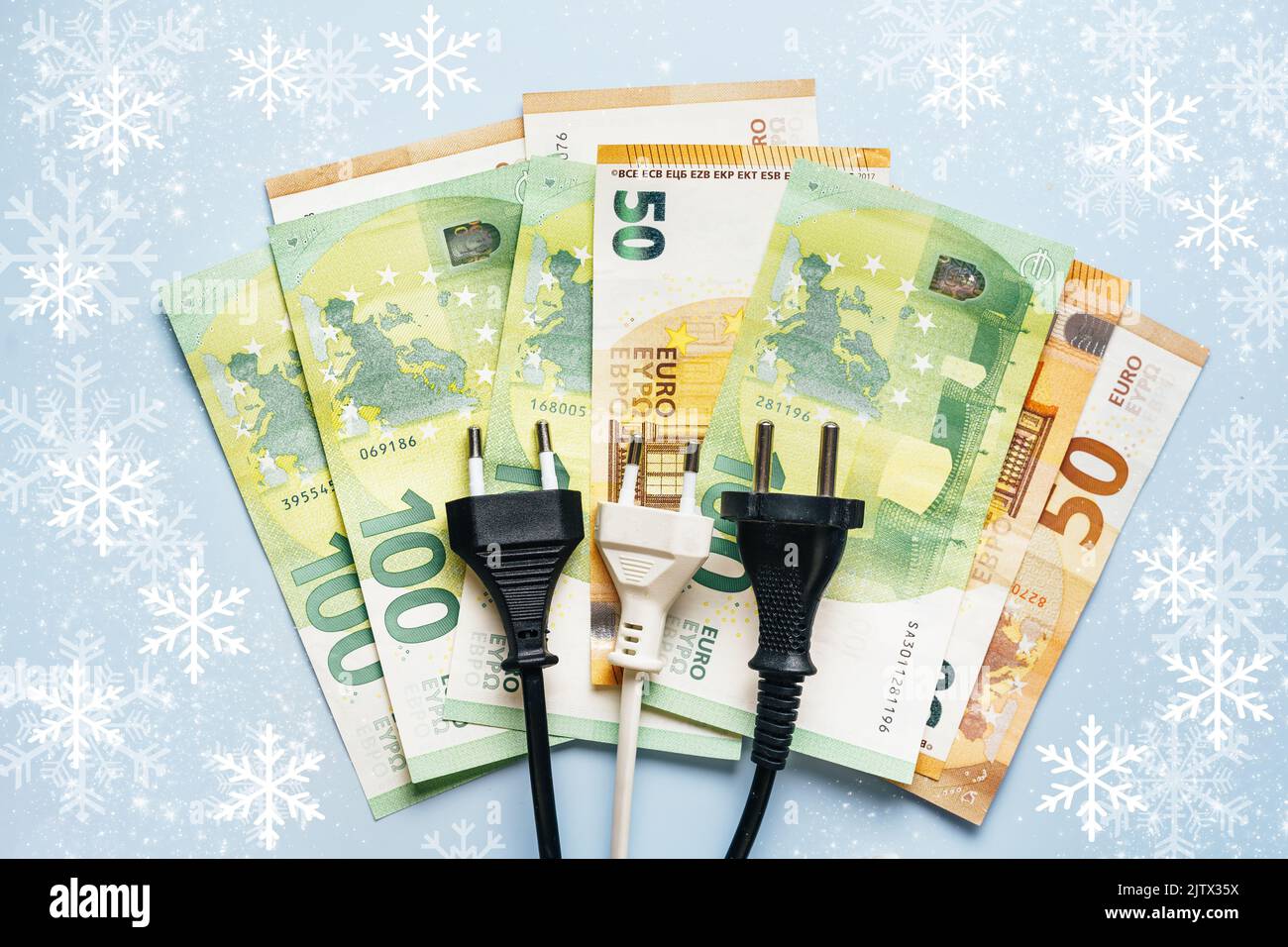 La spina elettrica si trova sulle banconote in euro che mostrano l'inflazione drastica sui costi dell'elettricità in inverno. Il concetto di crisi energetica in Europa. Vista dall'alto. Sfondo blu con fiocchi di neve Foto Stock