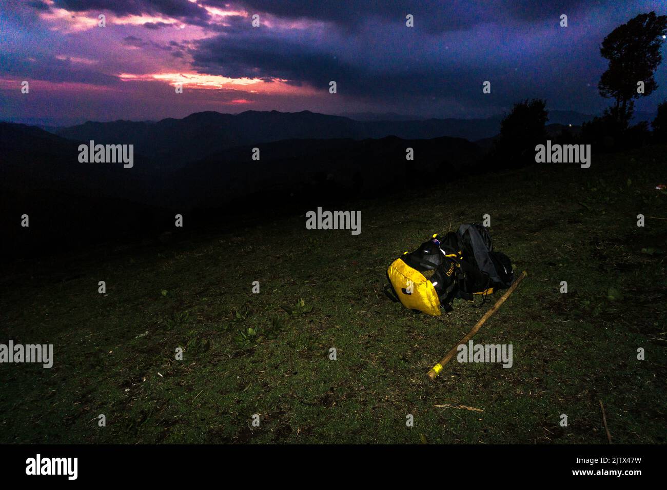 Marzo 3rd 2021 Uttarakhand India. Uno zaino e un bastone da passeggio sulla cima di una collina con un paesaggio colorato sullo sfondo durante il tramonto. Himalayan tr Foto Stock