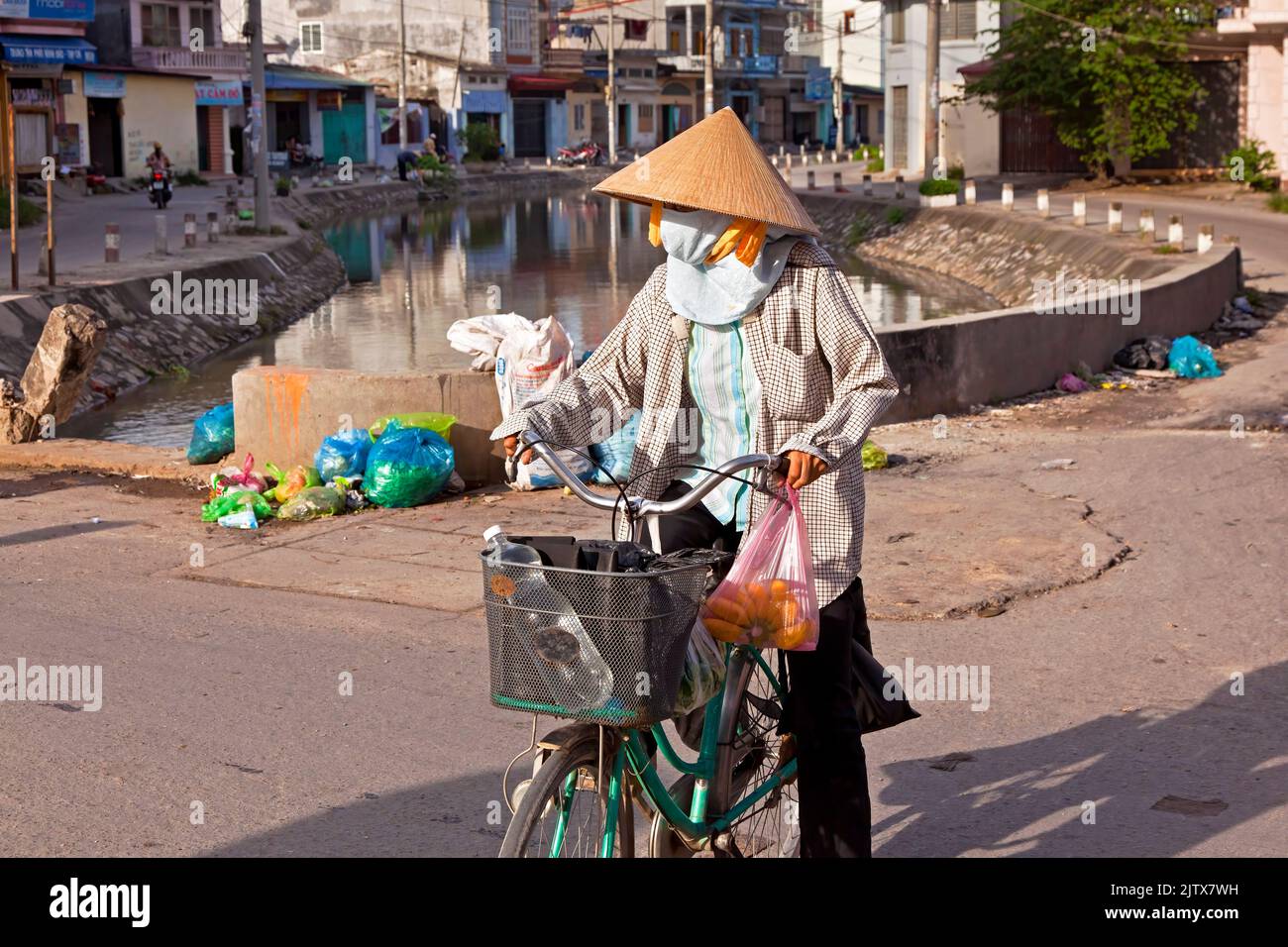 Signora vietnamita con bicicletta che indossa un cappello di bambù sul canale, Hai Phong, Vietnam Foto Stock