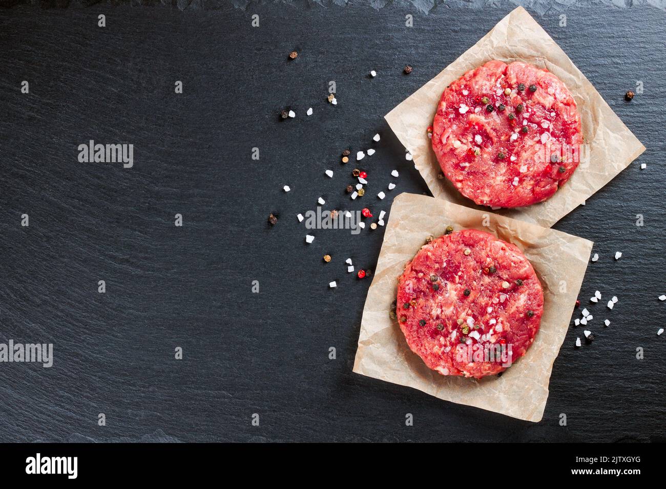 Hamburger di bistecca di manzo appena sminuzzato e crudo con spezie, su un tavolo di ardesia nera, spazio copia, vista dall'alto Foto Stock