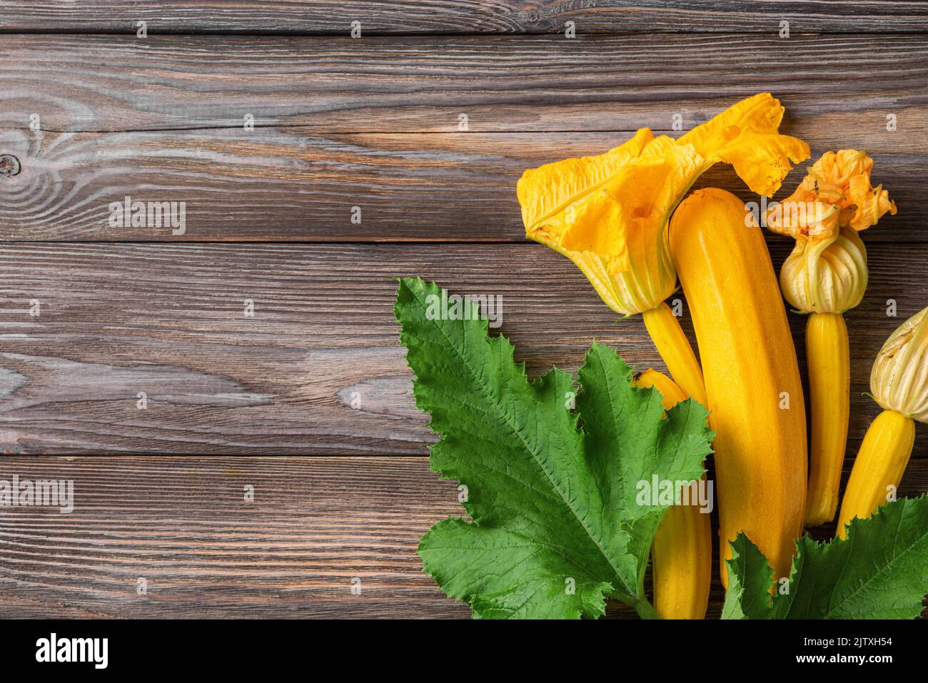 Zucchine fresche gialle o zucca con fiori su fondo in legno. Vista dall'alto con spazio di copia. Verdure fresche raccolte Foto Stock