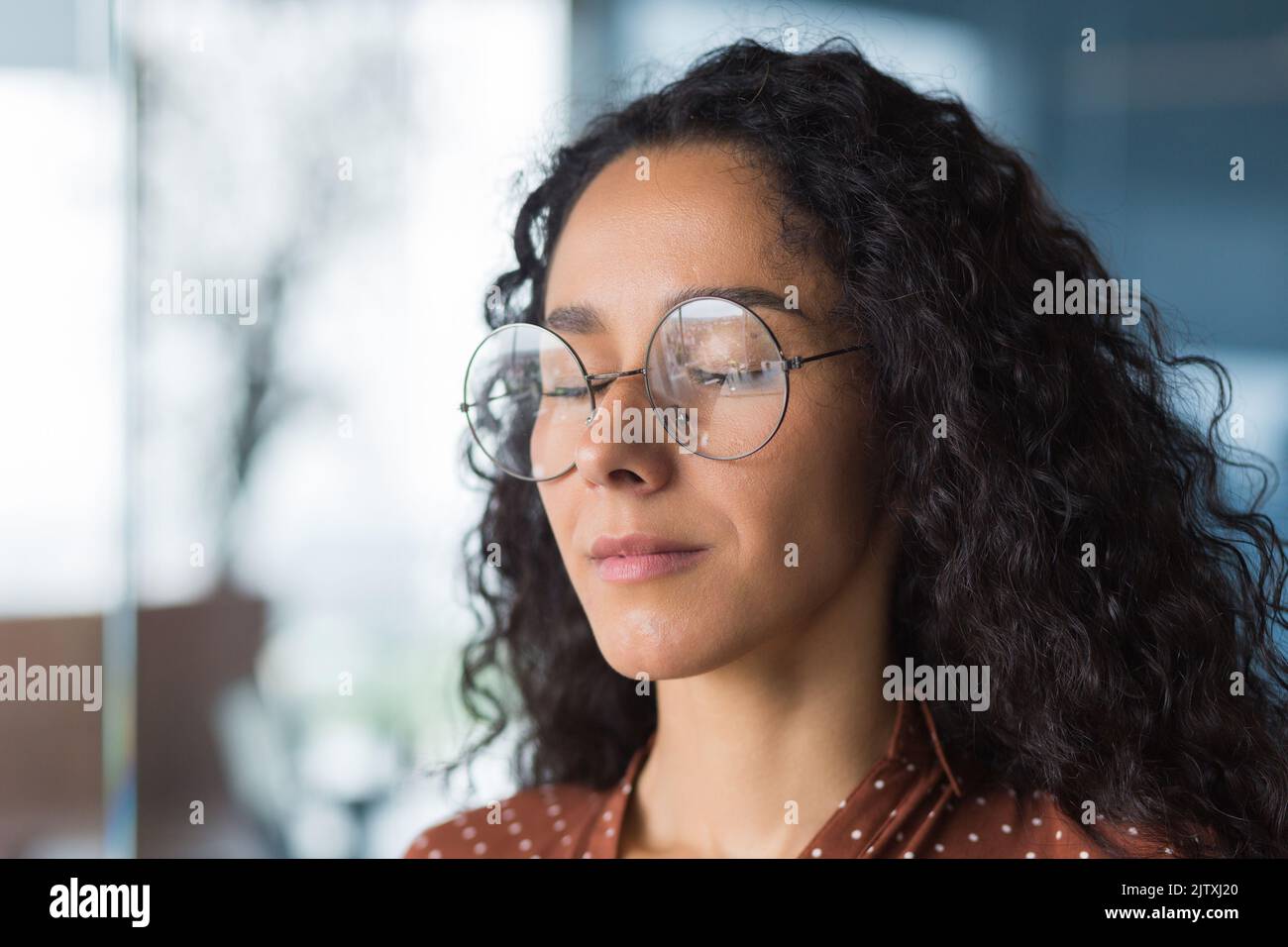 Primo piano ritratto femmina programmatore ingegnere sviluppatore con occhi chiusi in occhiali, sognando e visualizzando il risultato desiderato, donna d'affari che lavora in ufficio moderno, ispanico con capelli ricci in casual Foto Stock