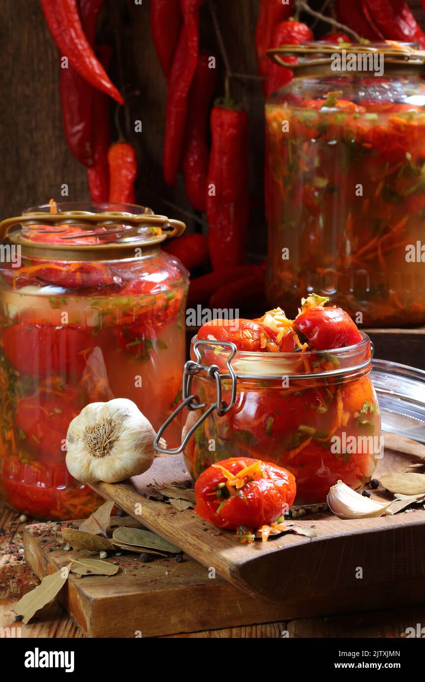 Pomodori rossi salati con verdure, farcitura speziata in vasetti su un tavolo di legno Foto Stock