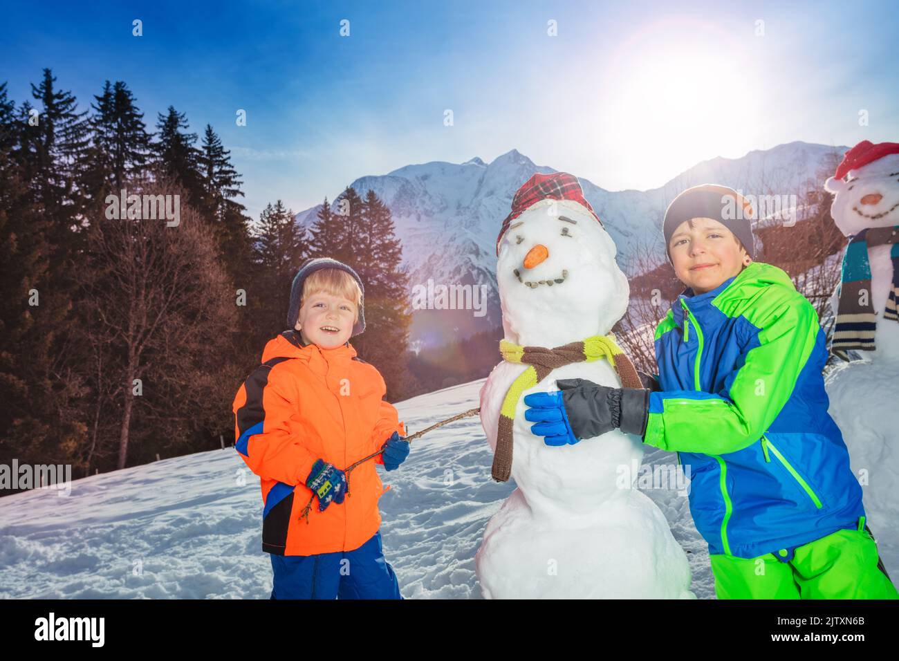 Due felici bambini sorridenti costruiscono e vestono il pupazzo di neve all'esterno Foto Stock