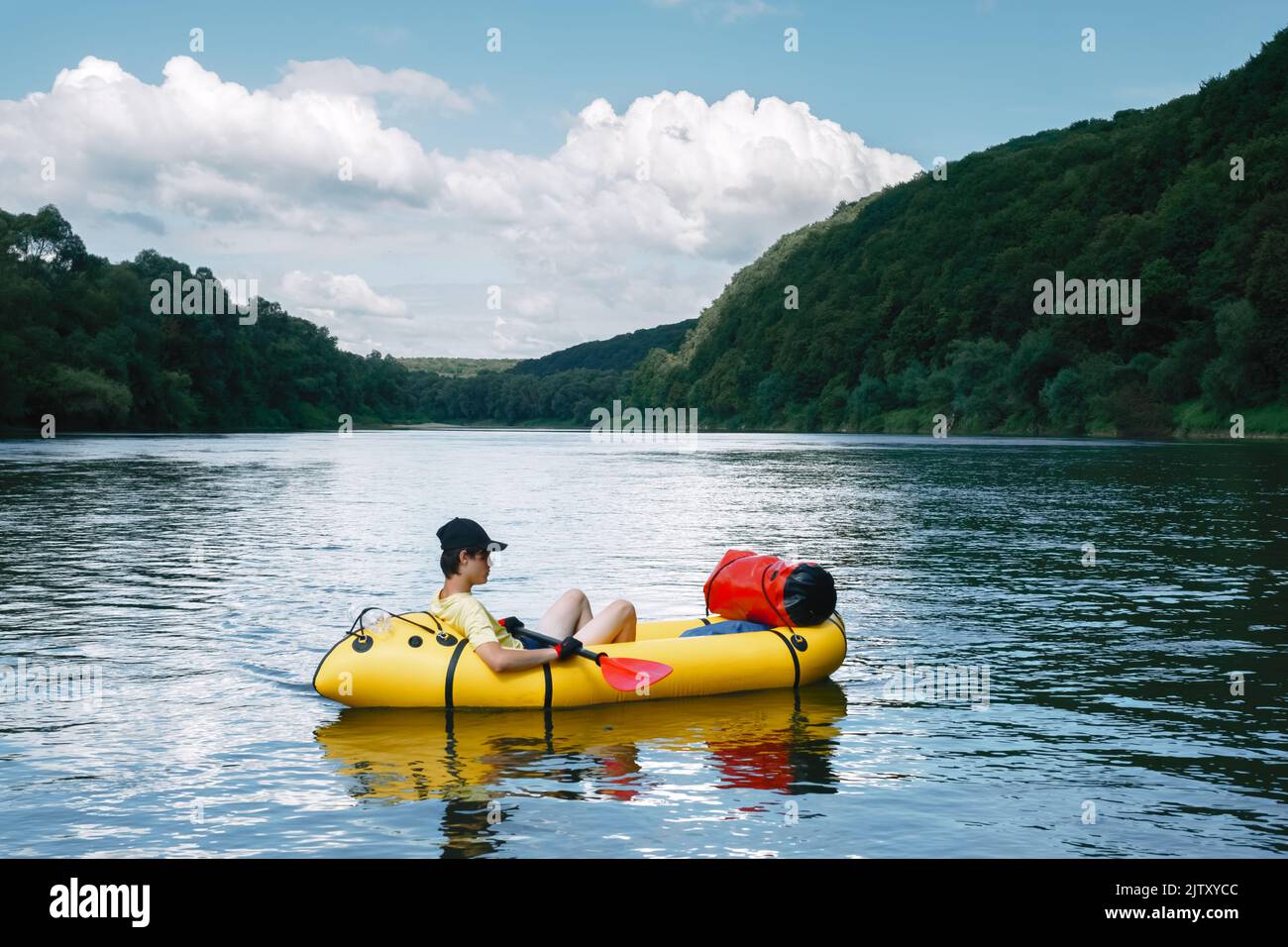 Turista su una barca di gomma di packraft giallo con padle rosso su un fiume di alba. Packrafting. Concetto di vita attiva Foto Stock