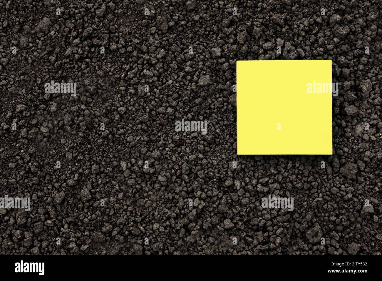 Giallo nota carta quadrato su suolo nero struttura terra primo piano. Giallo sticky note carta bianca terreno piano terra organica struttura. Mockup su suolo di terra Foto Stock