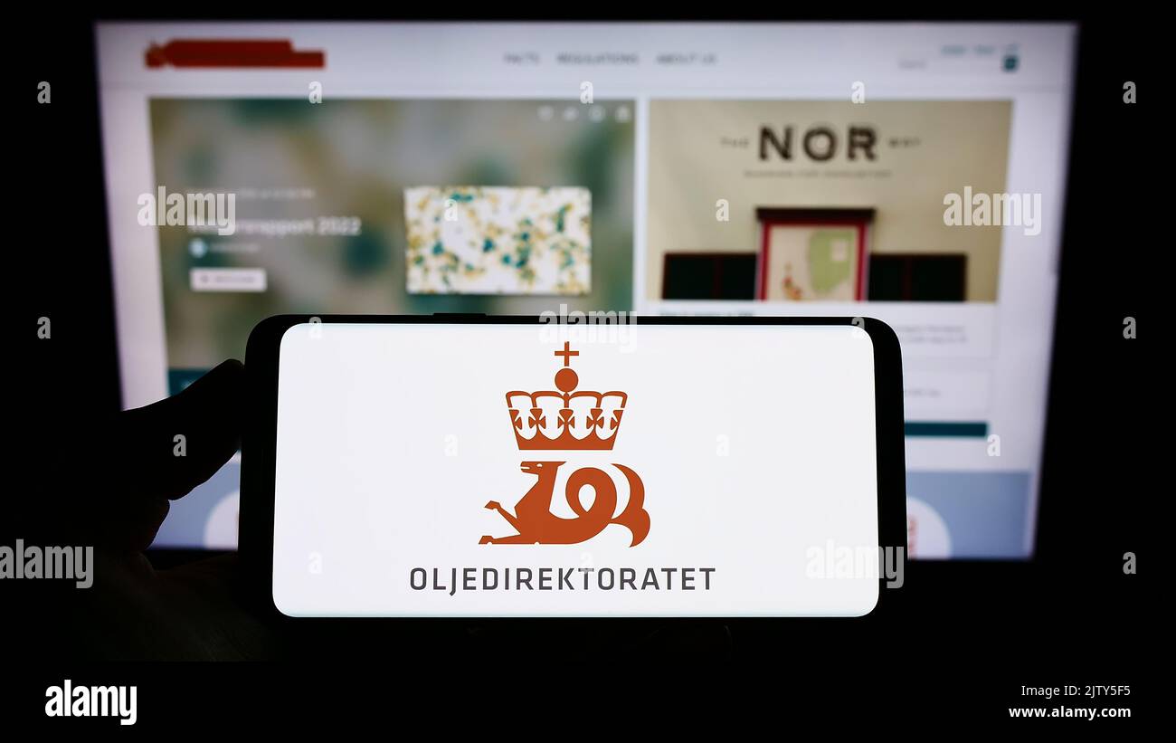 Persona che tiene uno smartphone con il logo dell'agenzia Norwegian Petroleum Directorate (NPD) sullo schermo di fronte al sito Web. Messa a fuoco sul display del telefono. Foto Stock