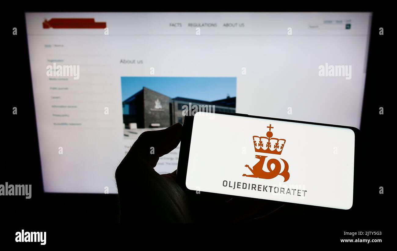 Persona che tiene il cellulare con il logo dell'agenzia Norwegian Petroleum Directorate (NPD) sullo schermo di fronte alla pagina web. Messa a fuoco sul display del telefono. Foto Stock