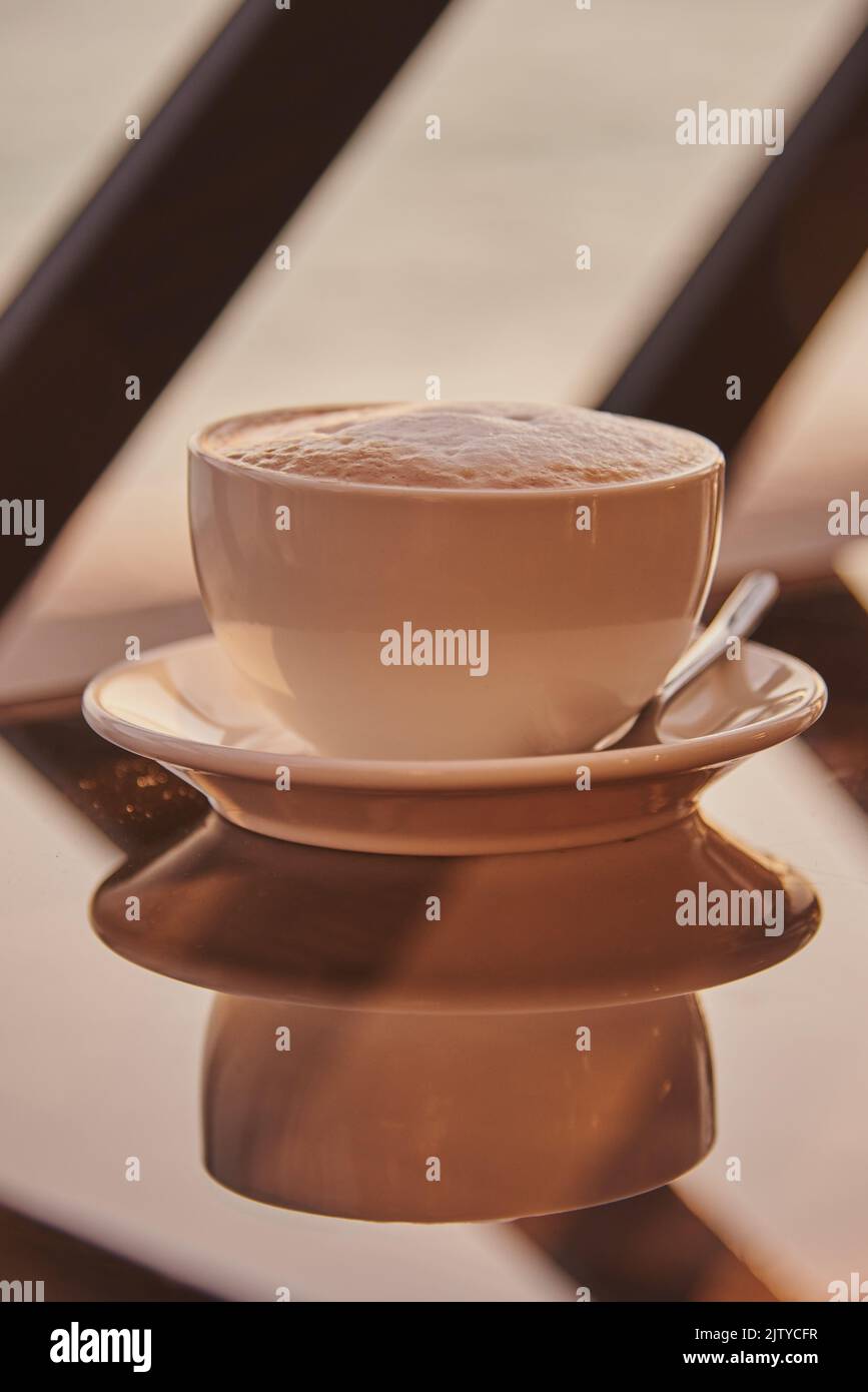 Una tazza di cappuccino su un tavolo di vetro contro il tramonto. Foto Stock