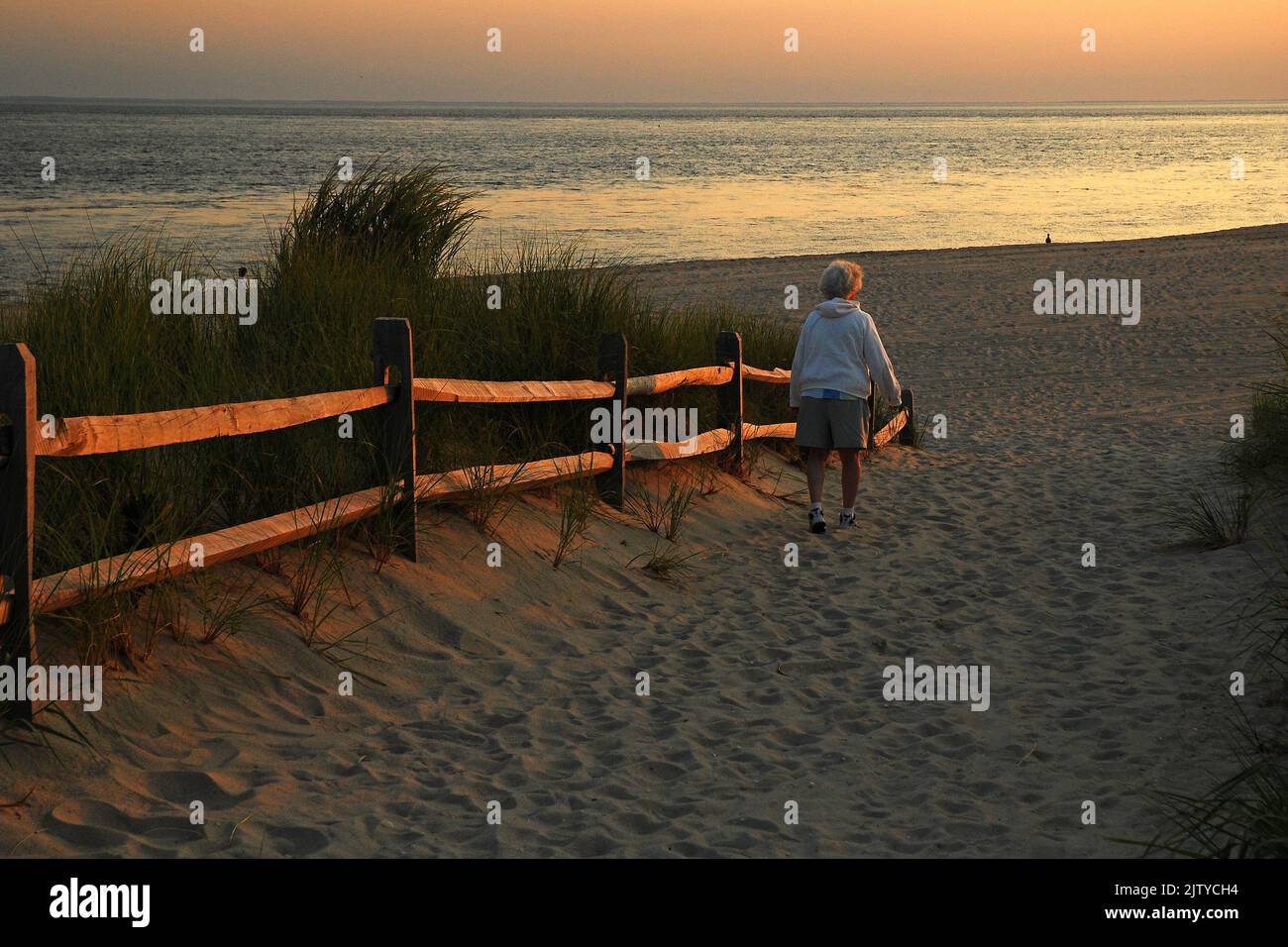 Una donna anziana solitudine cerca solitudine e tranquilla contemplazione come lei segue un percorso verso il mare vicino al tramonto a Cape May New Jersey Foto Stock