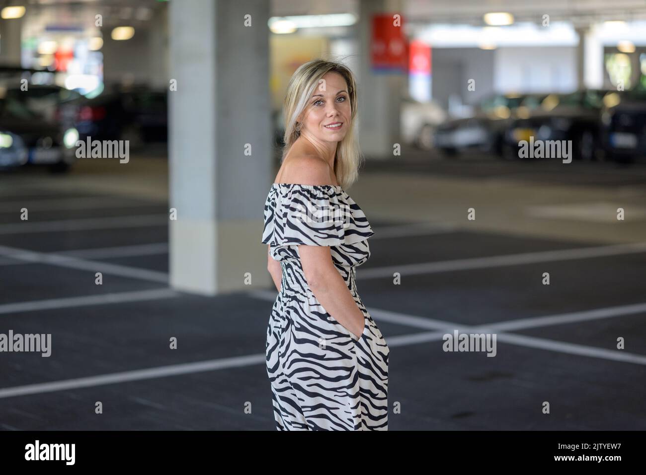 Donna attraente pausa di guardare indietro sopra la sua spalla come lei cammina attraverso un garage parcheggio ombreggiato Foto Stock