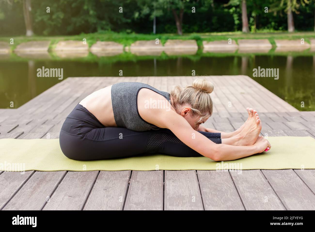 Una donna accanto a uno stagno nel parco fa yoga, facendo stretching. Foto Stock