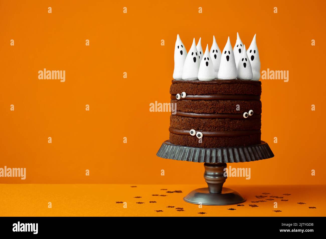 Torta di Halloween al cioccolato con fantasmi di meringa spettrale e occhi di caramella su uno sfondo arancione con copyspace a lato Foto Stock