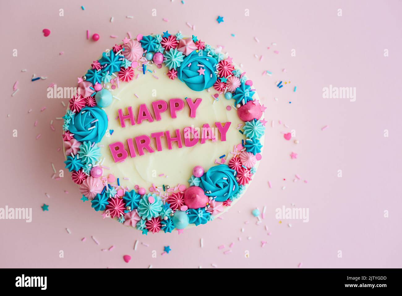 Torta di compleanno con colorato saluto di buon compleanno e spruzzi su uno sfondo rosa, vista dall'alto Foto Stock