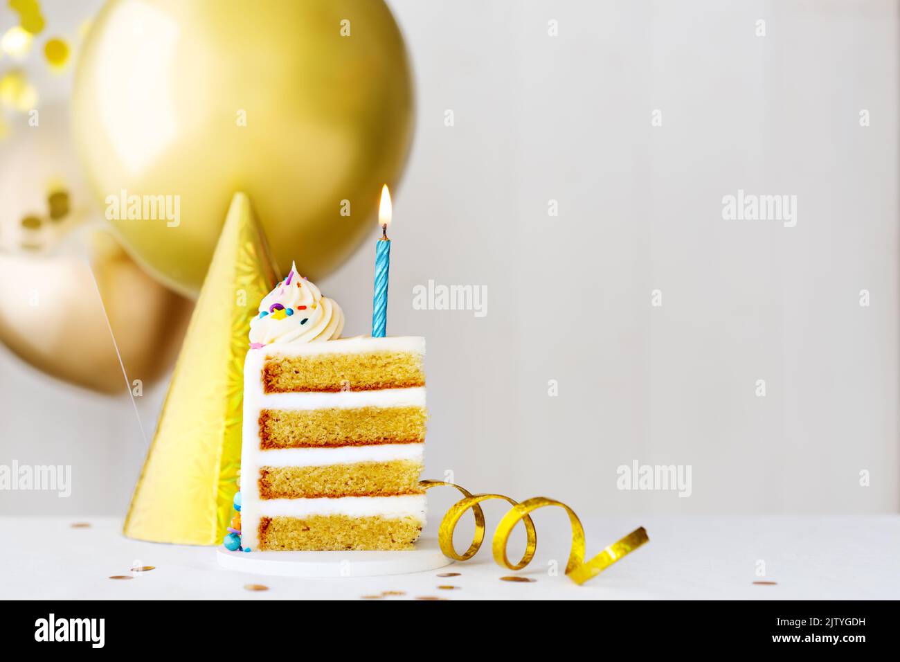 Fetta di torta di compleanno con una candela di compleanno blu e palloncini di compleanno d'oro Foto Stock