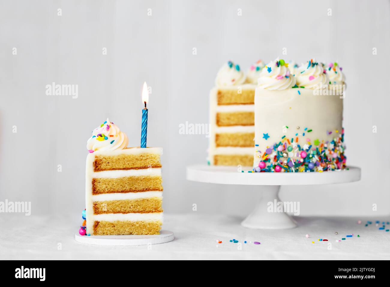 Torta di compleanno a fette con candela di compleanno blu e spruzzette colorate Foto Stock