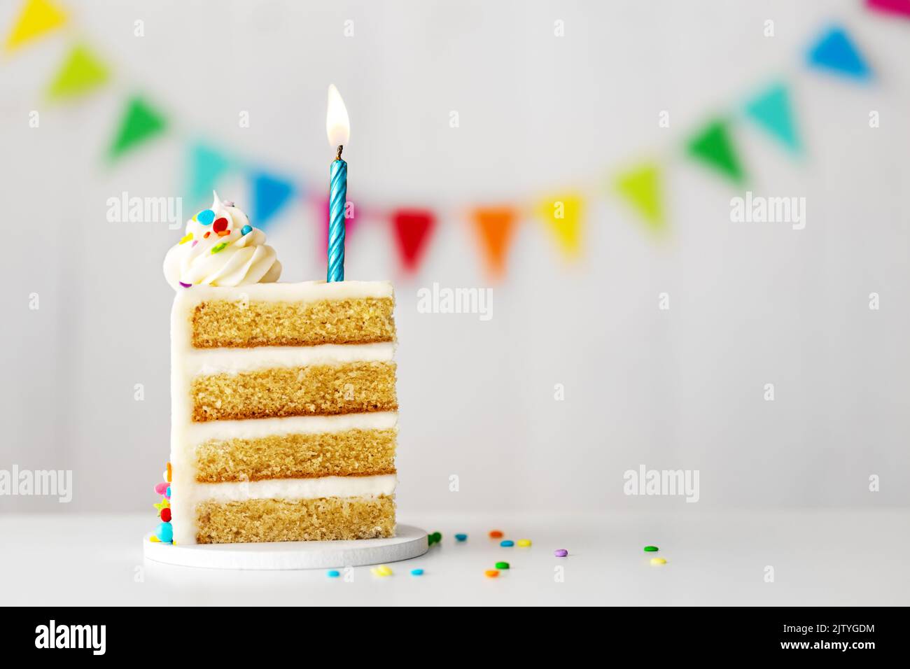 Fetta di torta di compleanno con candela di compleanno blu, spruzzette colorate e bunting celebrazione pronti per una festa di compleanno Foto Stock