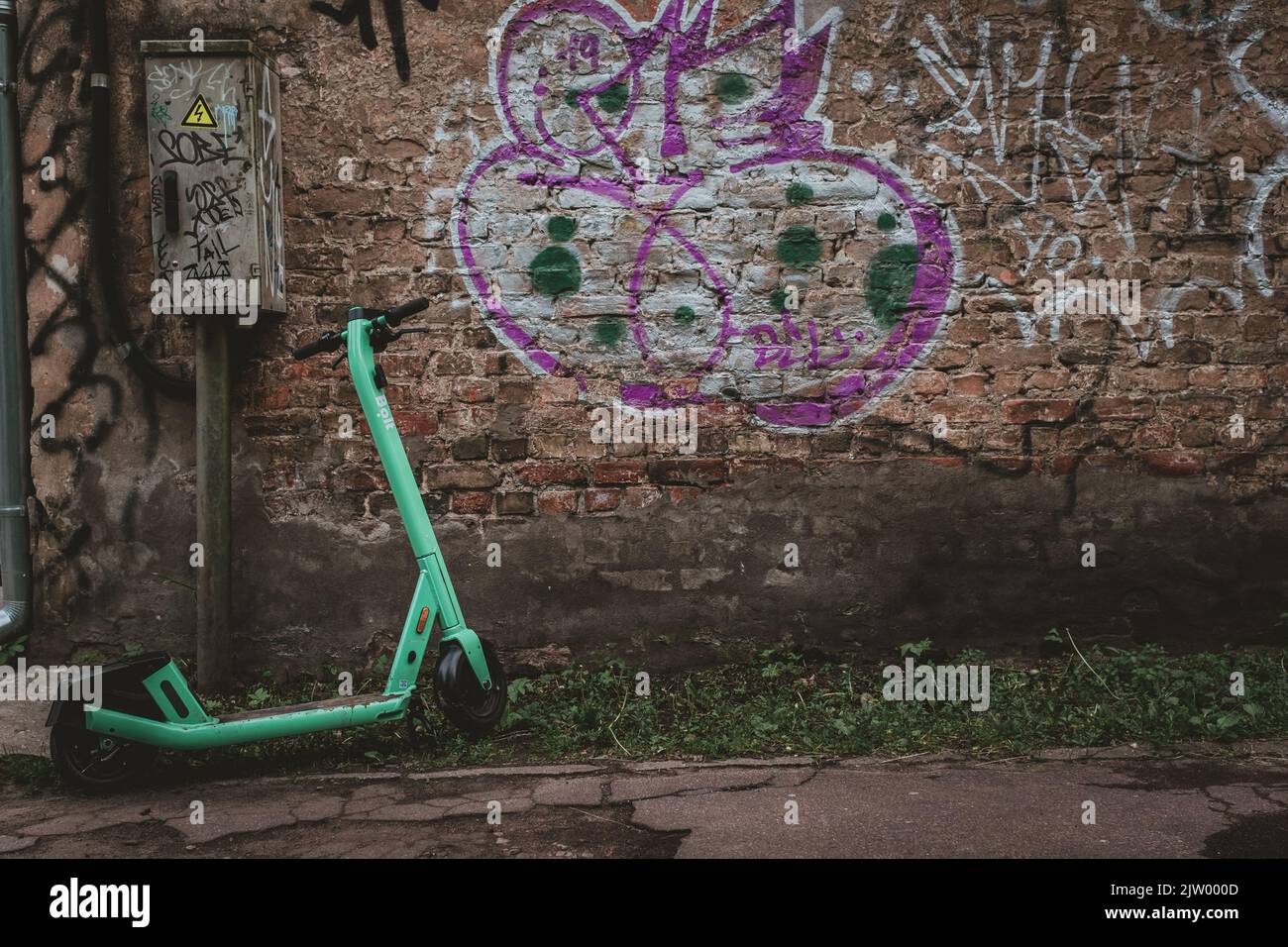 Scooter elettrico bullone parcheggiato vicino a cassetta elettrica con graffiti muro di mattoni coperti su uno sfondo. Foto Stock