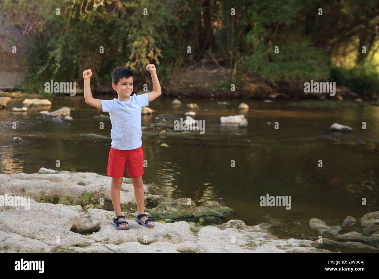 il bambino festeggia eccitatamente con i pugni alzati dal fiume. Divertimento nella natura Foto Stock