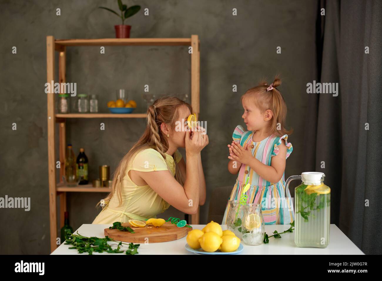 la mamma mostra le fette di limone invece degli occhi e degli stolti intorno con la figlia in cucina Foto Stock