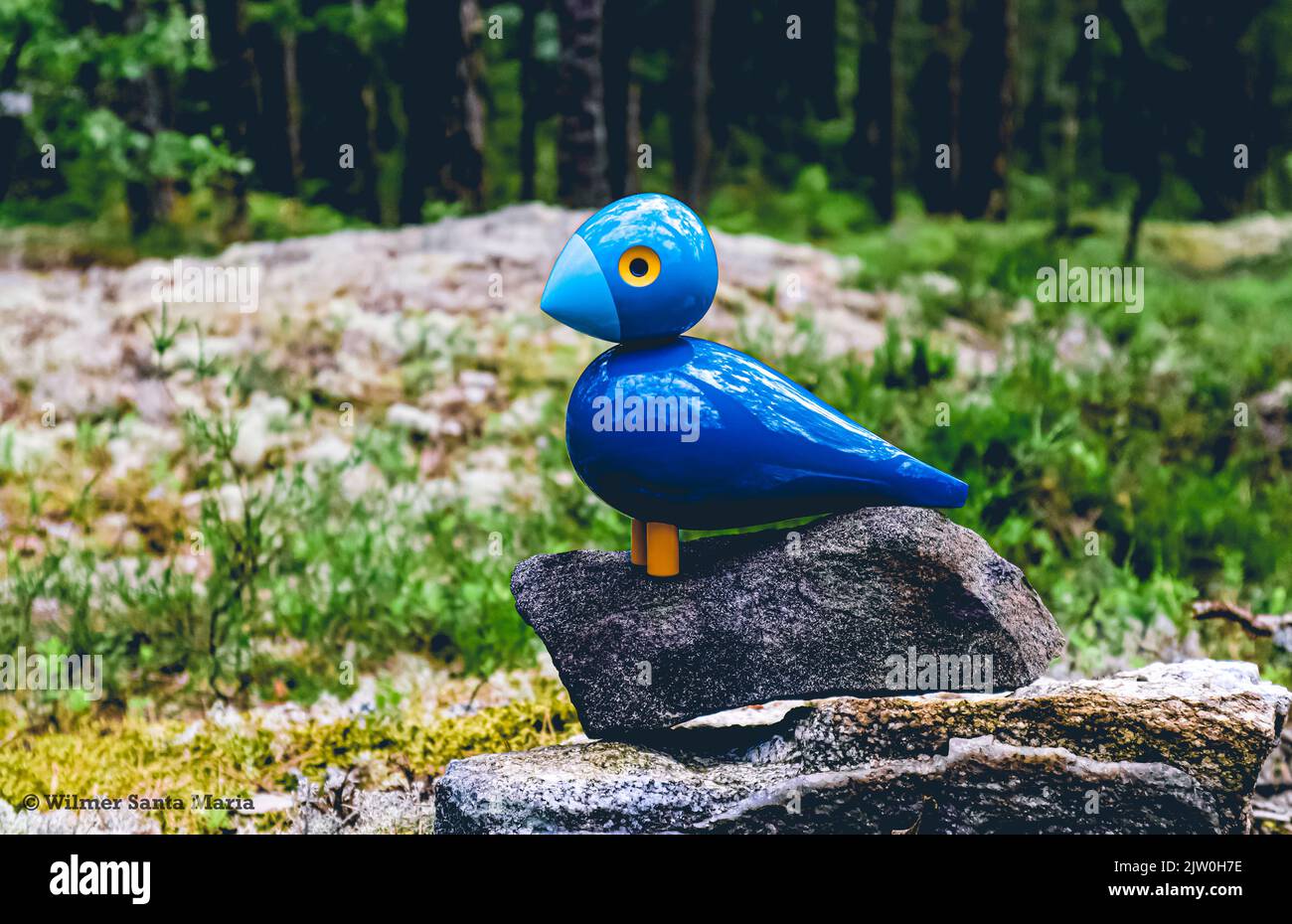 Vista panoramica di una figura decorativa in legno blu Kay Bojesen songbird (Sångfågel) seduta su una roccia nella foresta di Vilsta, Eskilstuna, Svezia. Foto Stock