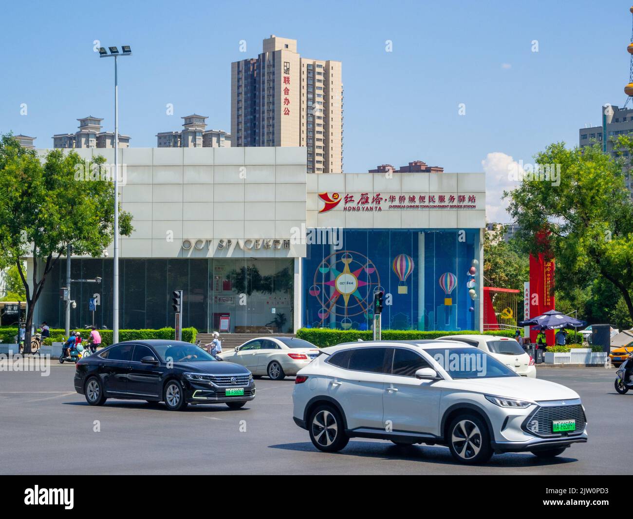 Auto moderne che guidano in un viale del centro. Un edificio d'affari con segni in lingua cinese è sullo sfondo. Foto Stock