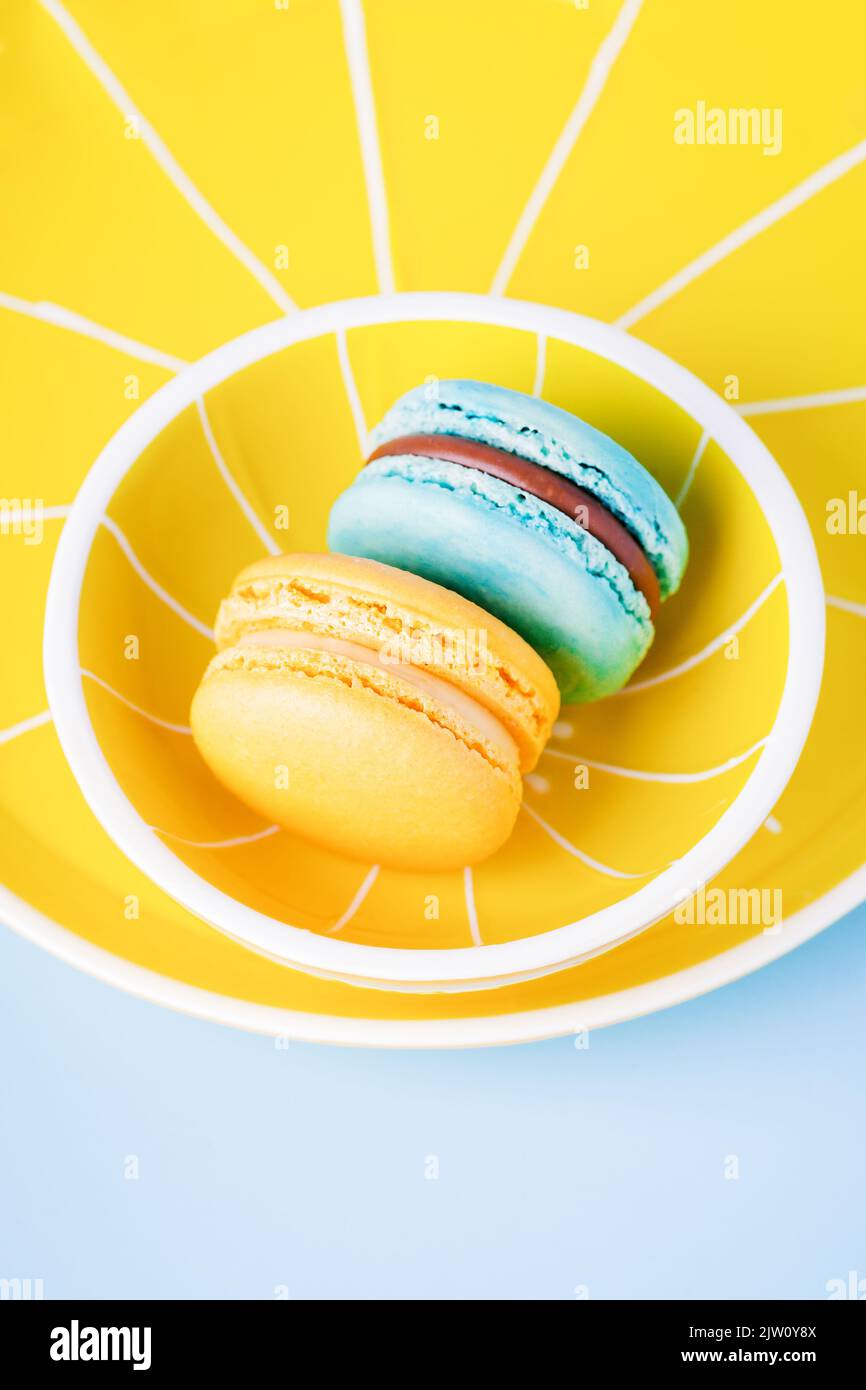 Macaron blu e giallo su piatto giallo e fondo blu Foto Stock
