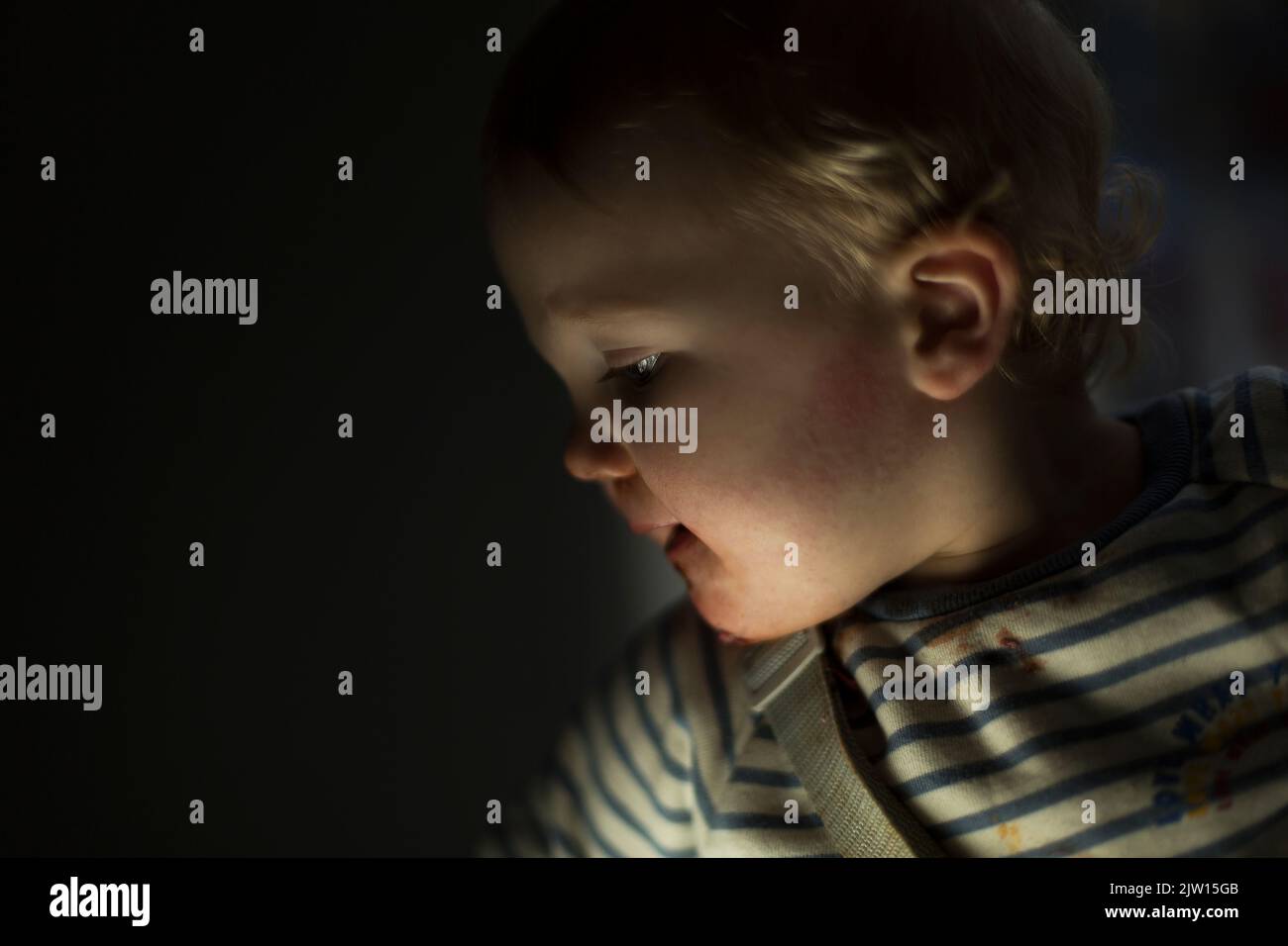 Toddler caucasico maschio guarda lateralmente con una luce più bassa, creando un aspetto leggermente drammatico. Foto Stock