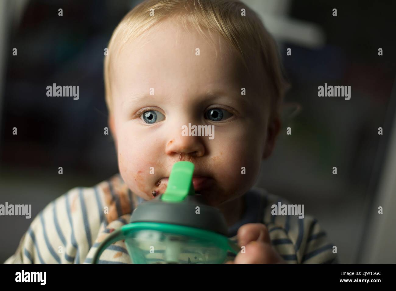 Ragazzino che prende un drink durante la cena e guarda lontano dalla macchina fotografica. Foto Stock