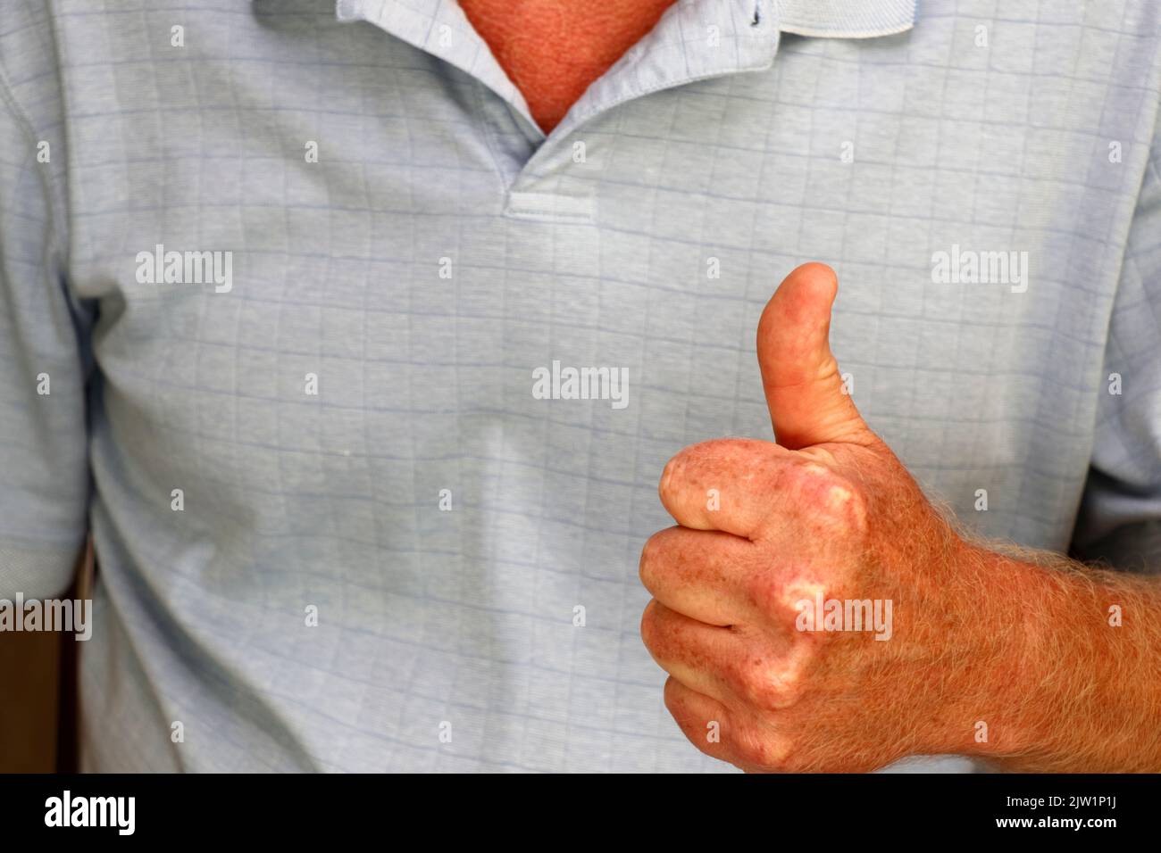 La mano sinistra di un maschio bianco adulto in una camicia blu che esprime l'approvazione con un segno della mano di pollice in su primo piano. Pollice su mano segno mostrato da una mano sinistra di Foto Stock