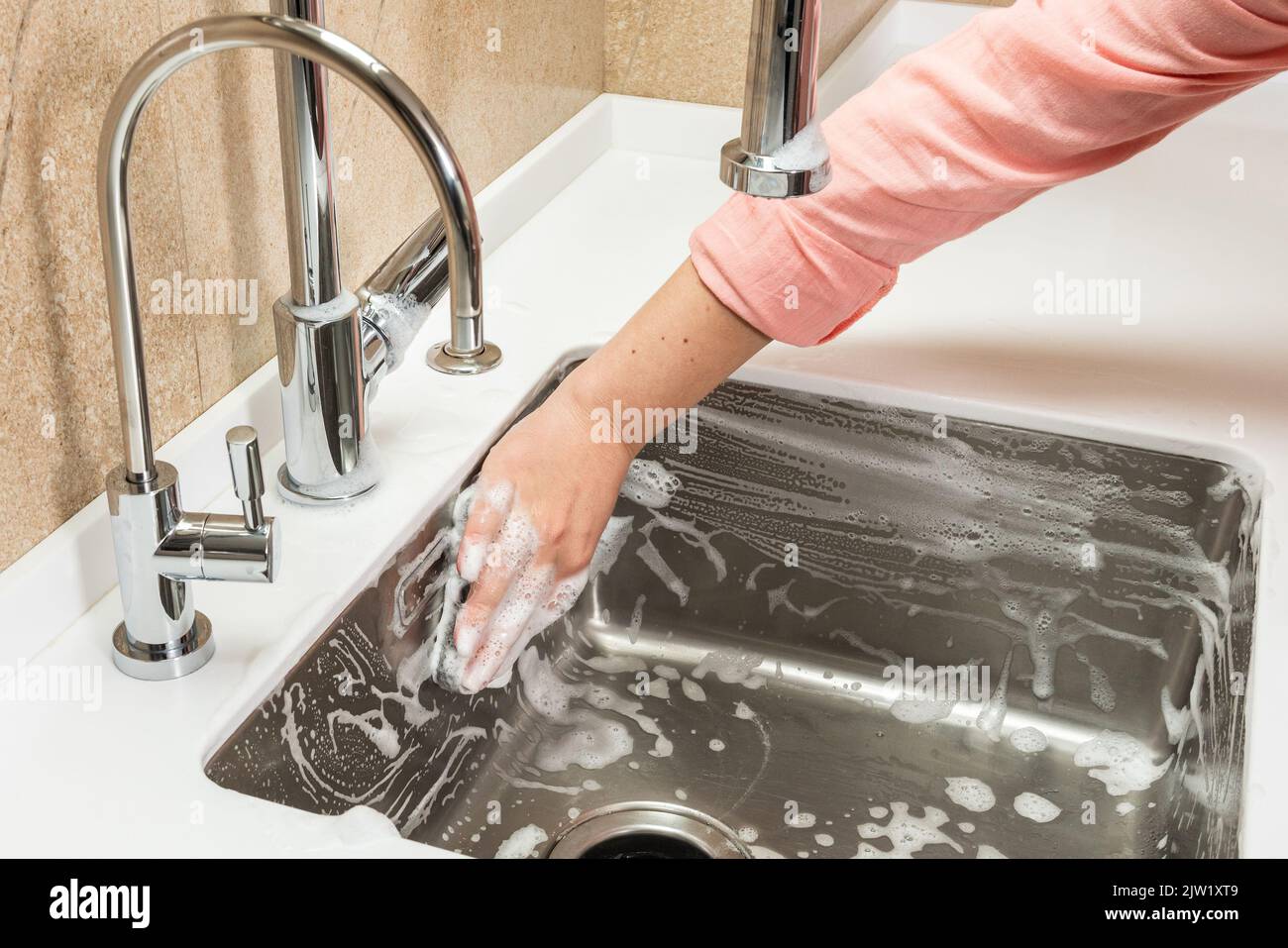 Schiuma e mano con spugna di pulizia sul lavello da cucina Foto Stock