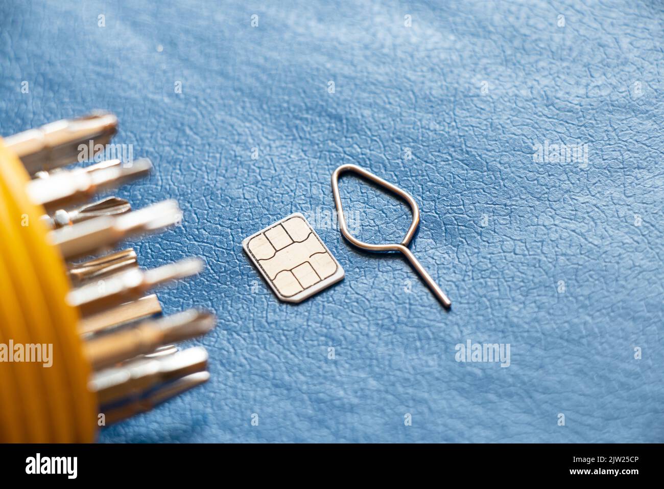 La scheda sim con pin e un set di cacciaviti si trovano su sfondo blu, riparazione e diagnostica di telefoni, assistenza e manutenzione Foto Stock
