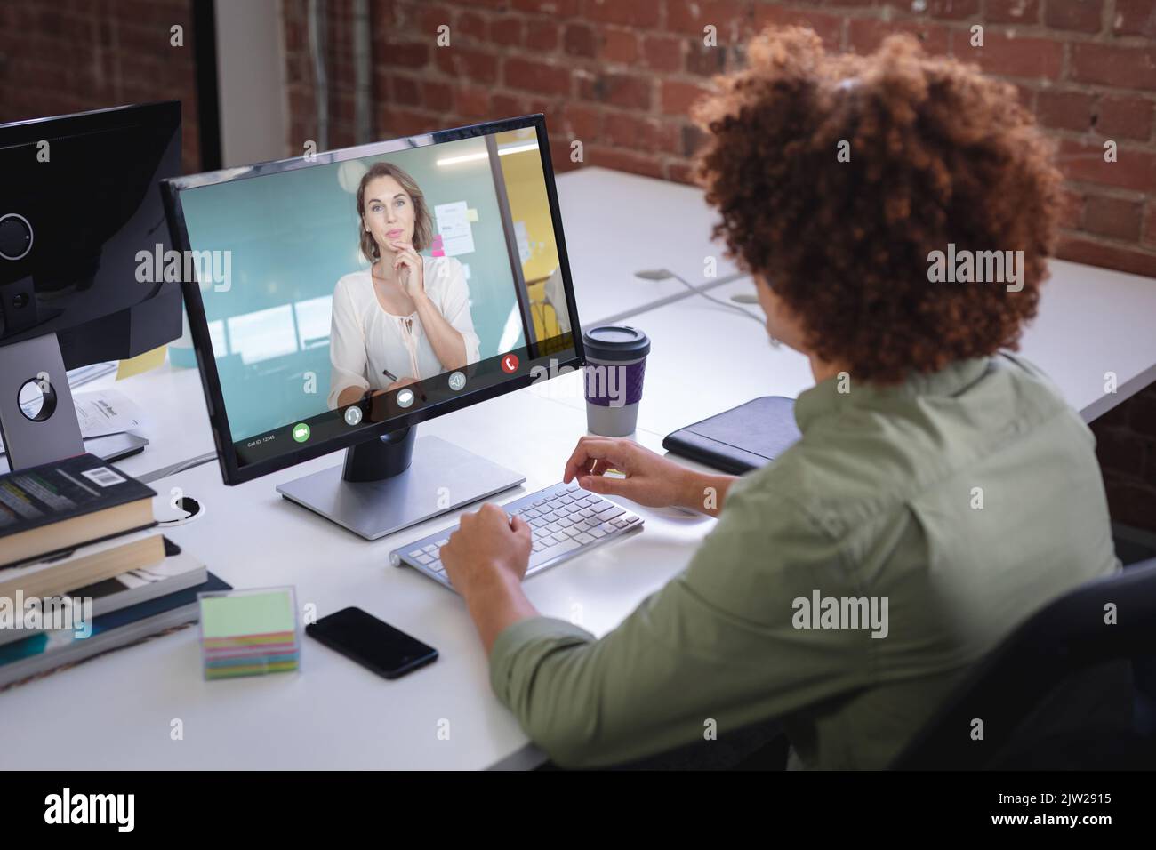 Biracial afro uomo d'affari che lavora online con la donna d'affari caucasica attraverso il pc desktop in ufficio Foto Stock