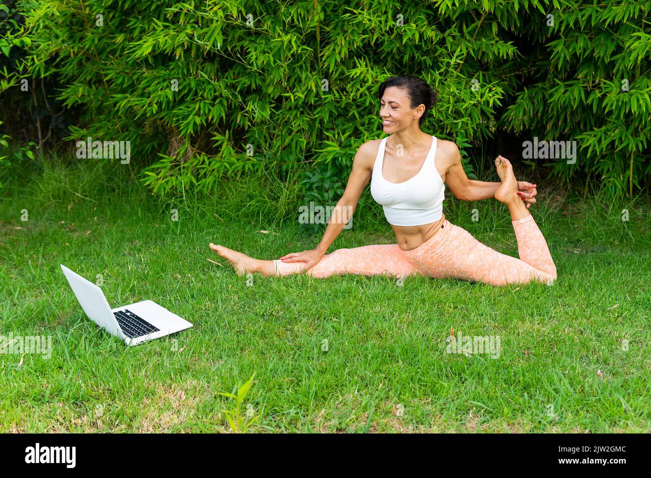 Dall'alto corpo completo di donna attiva che pratica Eka Pada Raja Kapotasana D postura durante l'allenamento di yoga online nel parco Foto Stock