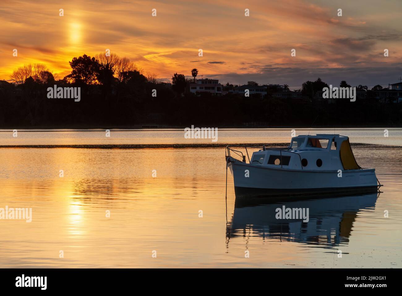 Una piccola barca sulle tranquille acque di un porto al tramonto Foto Stock