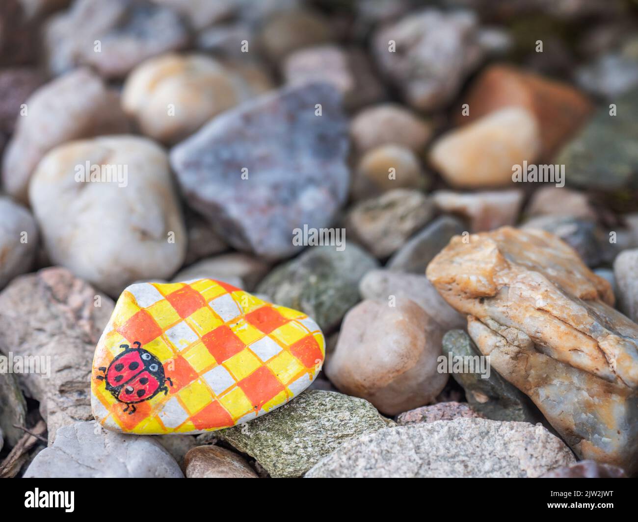 Ladybug dipinto su ciottoli piccoli, gioco di sentiero per bambini. Ciottoli nascosti con immagini dipinte nella destinazione di vacanza. Foto Stock