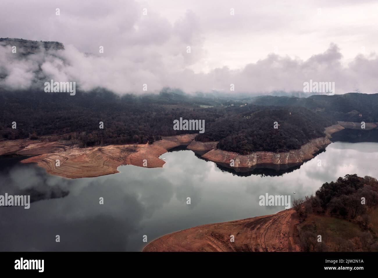 Vista del crinale di montagna coperto di nubi grigie sulla riva del fiume tranquillo con acqua riflettente in natura Foto Stock