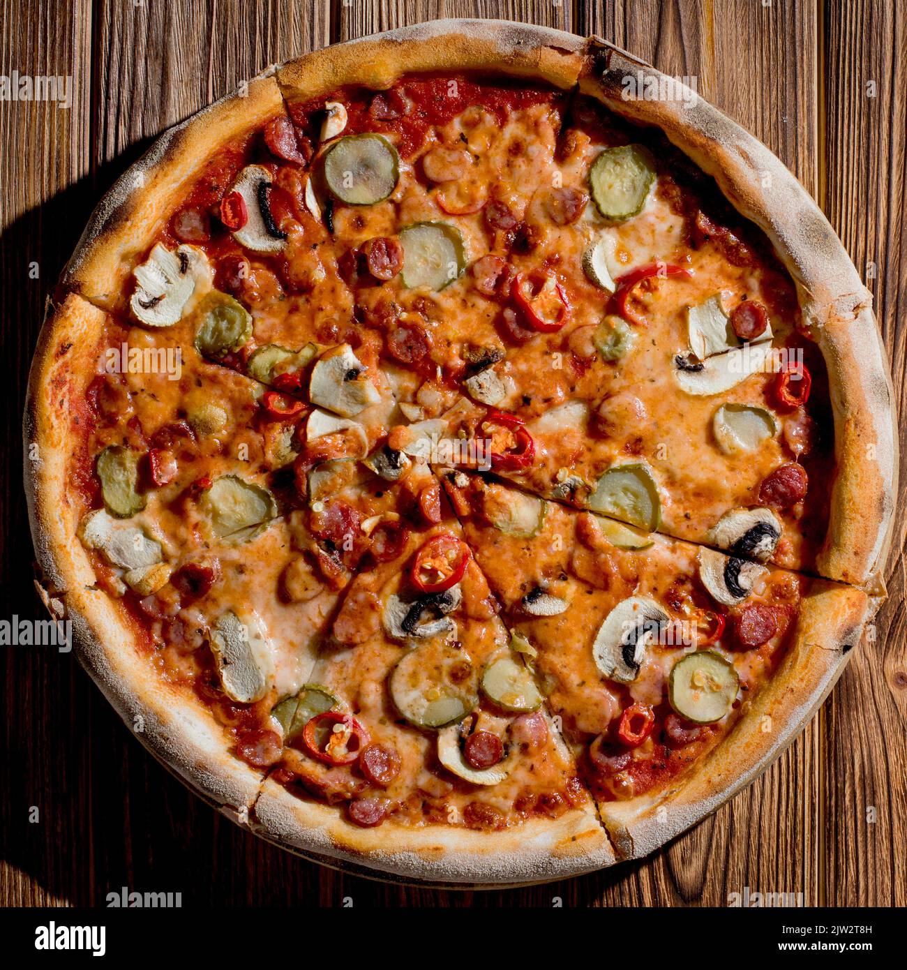 Pizza appetitosa con salsicce da caccia, mozzarella, cetrioli sottaceto, peperoncino su una base di pomodoro su fondo di legno. Foto Stock