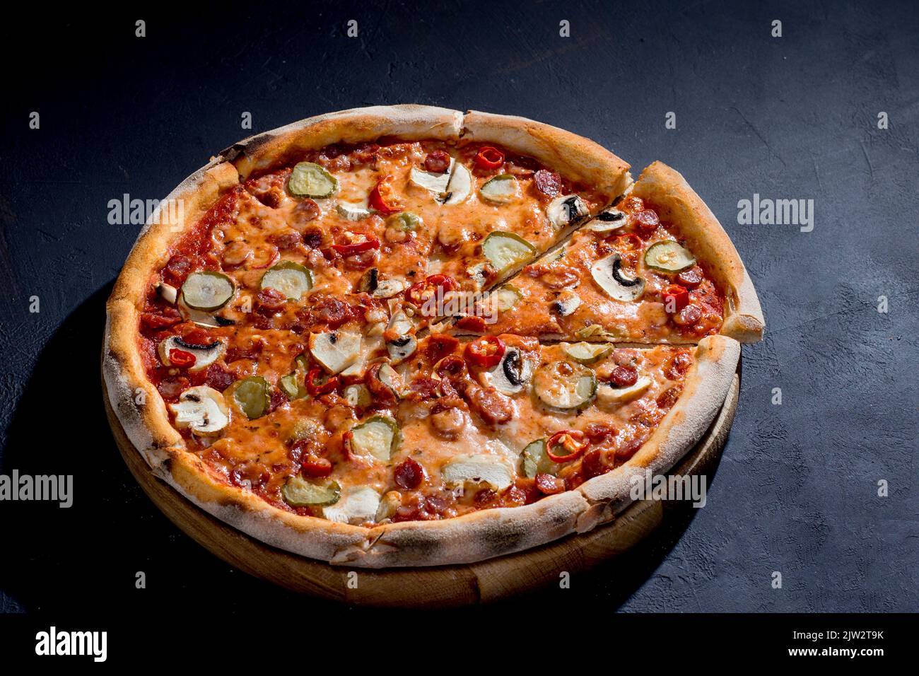 Pizza appetitosa con salsicce da caccia, mozzarella, cetrioli sottaceto, peperoncino a base di pomodoro su fondo nero. Foto Stock