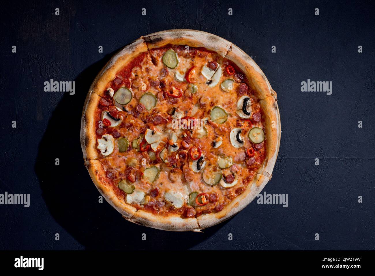 Pizza appetitosa con salsicce da caccia, mozzarella, cetrioli sottaceto, peperoncino a base di pomodoro su fondo nero. Foto Stock