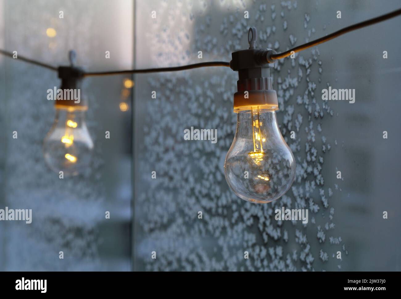 Semplice lampadina decorativa appesa su un balcone durante una giornata fredda. Vetro con cristalli di ghiaccio sullo sfondo. Energia, crisi energetica, elettricità. Foto Stock