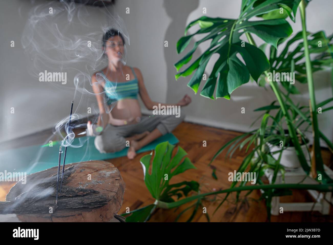 Donna incinta siede su un tappetino yoga in una posa di meditazione. Donna incinta che fa esercizi di yoga a casa. Sala incenso per rilassarsi durante lo yoga. Dur. Yoga Foto Stock