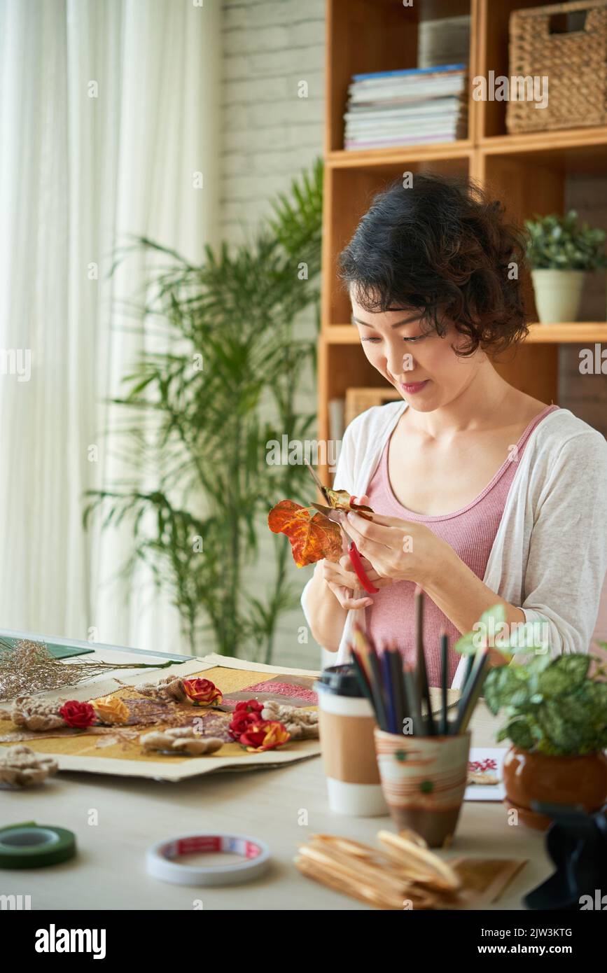 Giovane donna vietnamita sorridente che taglia fiori secchi per fare collage Foto Stock