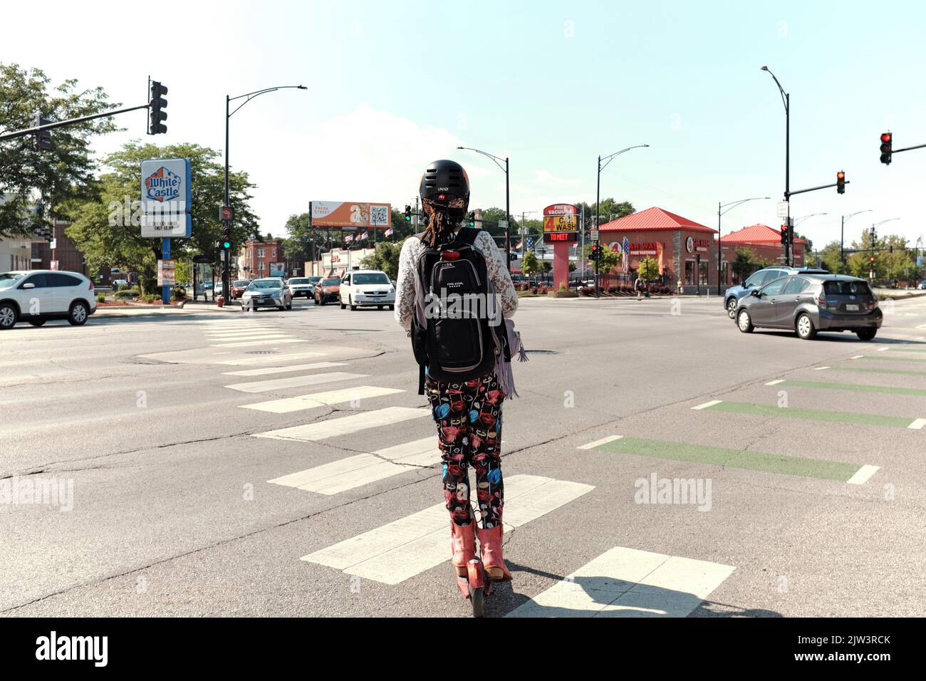 Donna con casco fa un giro in scooter attraverso North Clark Street all'incrocio con North Ridge nel quartiere di Chicago, Illinois Andersonville. Foto Stock