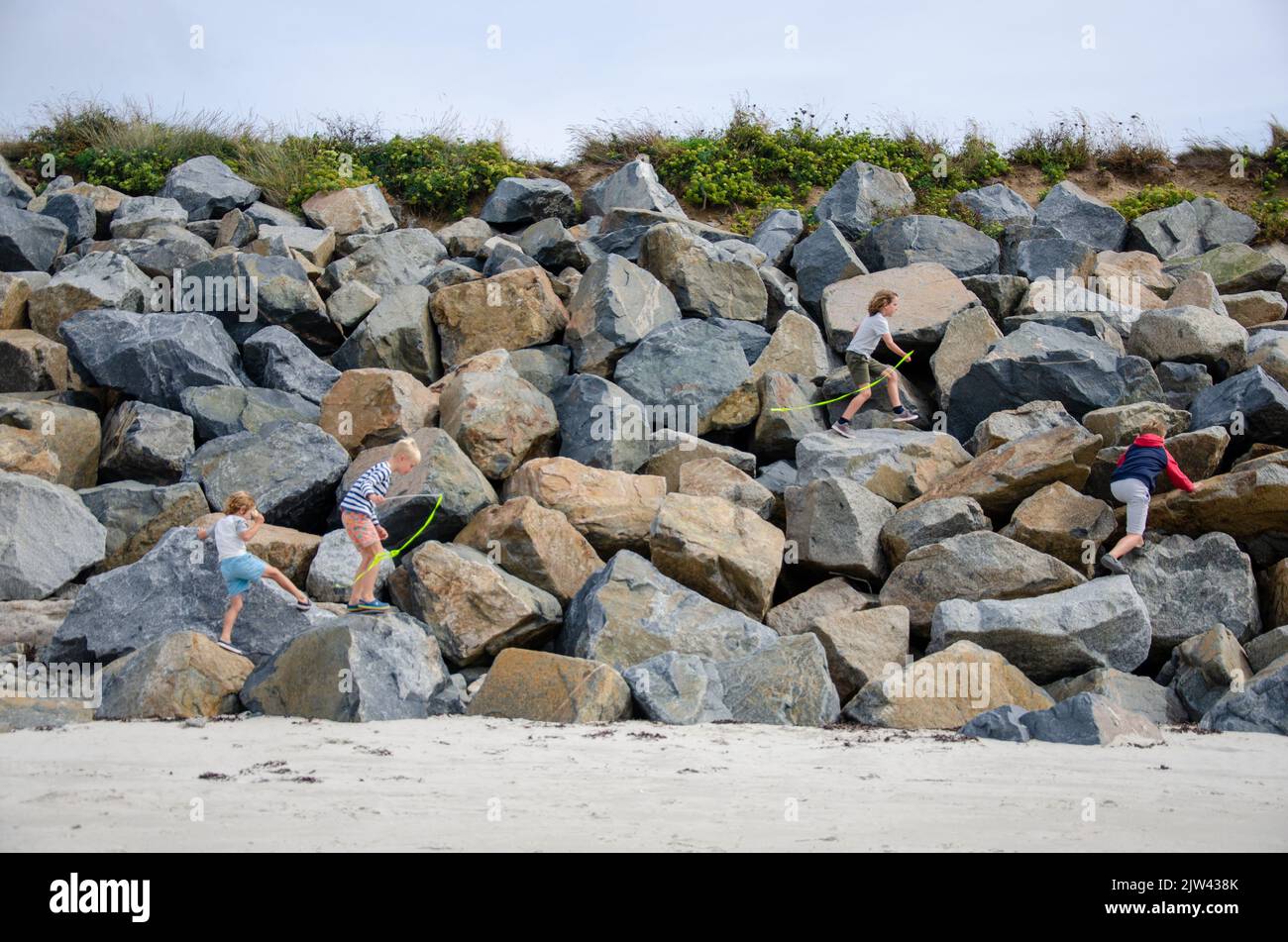 Quattro ragazzi che corrono insieme lungo la spiaggia di Guernsey, Regno Unito Foto Stock