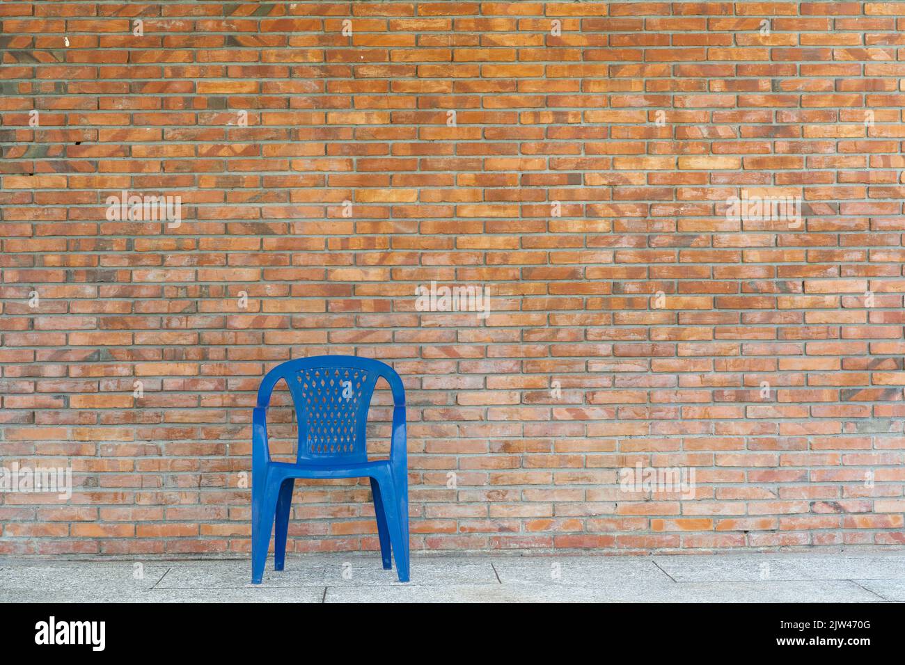 Sedia di plastica blu singola contro il muro di mattoni di argilla semplice Foto Stock